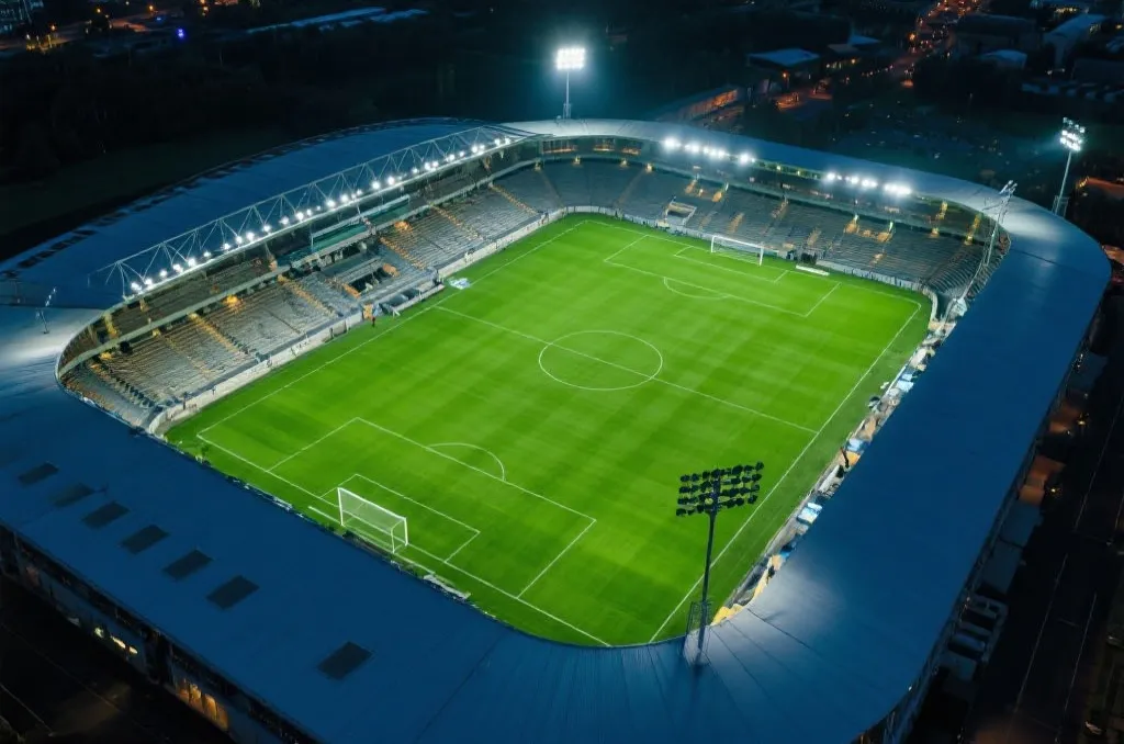 An aerial view of a generic modern football stadium with bright lights at dusk